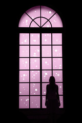 Woman standing and looking at lovely snowfall through big closed window and dreaming about Christmas. Conceptual Christmas or New Year Holiday woman silhouette background.