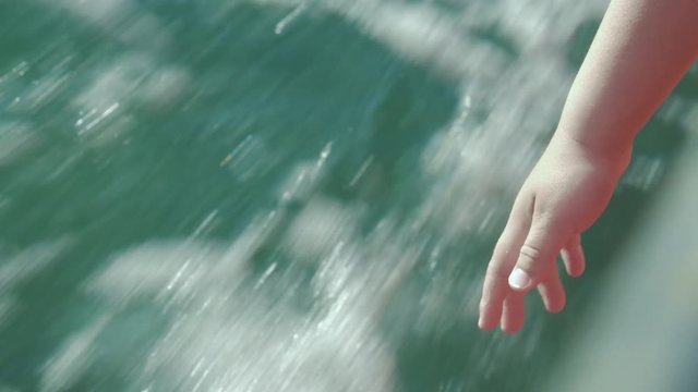 Close-up shot of a child pulling hand to water from the sailing boat. He wants to feel splashes on high speed