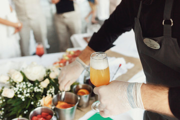 Waiter holds glass with orange drink and takes slices of fruits