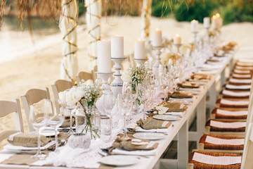 Long dinner table prepared for wedding party stands under beach