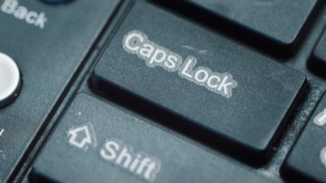 Extreme close up of a finger pressing 'caps lock' on a keyboard.