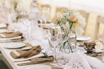 Wineglasses stand on dinner table with white flowers and flaxen