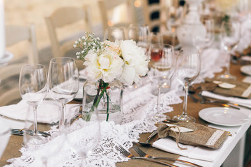 White peonies stand in bottles on dinner table covered with flax