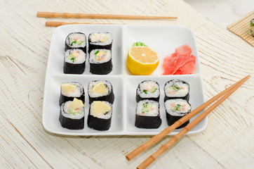 Square plate with a set of rolls on a wooden table. Chopsticks, ginger, lemon. Side view