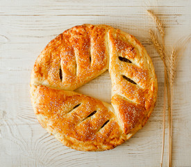 Round pie with sesame seeds on a light wooden background, ears of wheat