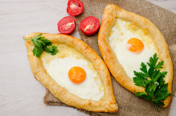 Two khachapuri with egg, parsley and tomatoes on sackcloth, top view