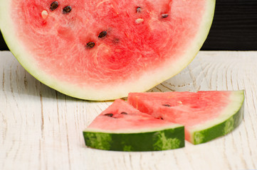 Halves cut watermelon slices on a light wooden table, close-up