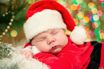 Portrait of newborn baby in Santa clothes lying under Christmas tree.
