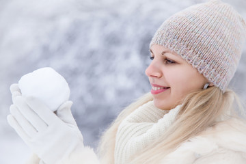 Woman wearing soft fur coat and enjoying a beautiful winter day and playing with snowball in the...