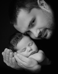 Daddy hugs his newborn baby. Father 's love. Close-up portrait on a black background
