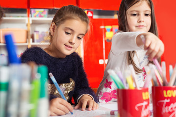 Two little girls drawing on paper at table