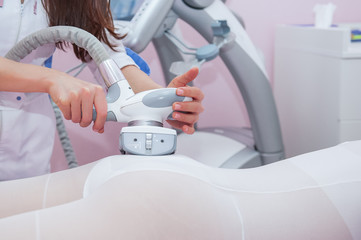 Parts of female body in special white suit having anti cellulite massage with spa apparatus