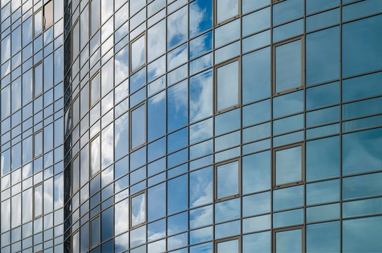 Skyscraper mirror glass surface reflecting cloudy sky, curvy surface