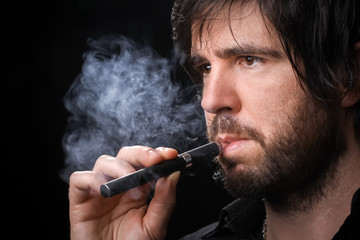 Young man smoking electronic cigarette on black background