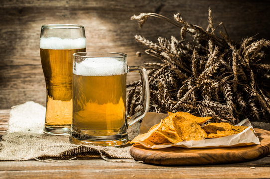 Mug, glass of beer with wheat spikelets , chips on board