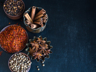 Various spices - cinnamon, star anise, cloves, saffron, allspice in a bowl on a dark background
