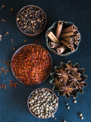 Various spices - cinnamon, star anise, cloves, saffron, allspice in a bowl on a dark background

