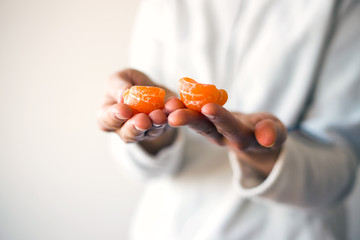 Woman in white pullover holding half of mandarin in hands