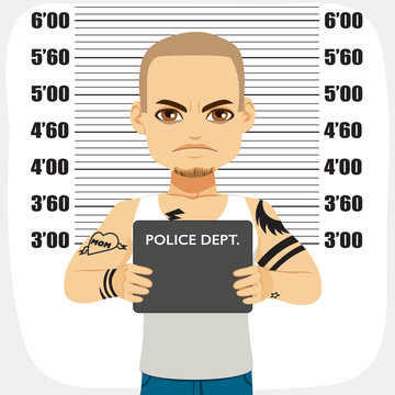 Dangerous male criminal with tattoos holding mugshot