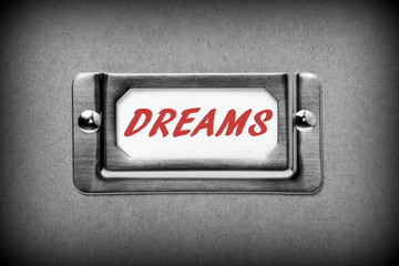 The word DREAMS in red text on a drawer label index card from a filing cabinet as a reminder not to file away your ambitions in a draw and forget them