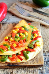 Vegetable omelet on a wooden board. Delicious fried omelet stuffed with red and green bell peppers and corn. Simple vegetarian breakfast omelet recipe. Vintage style. Closeup
