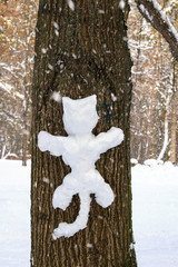 Fun snowman on pine trunk in the form of cat, winter snowfall day.
