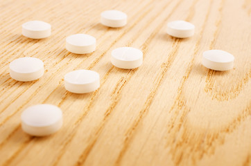Fototapeta na wymiar Pharmacy theme. White Pills lying on a Wooden Surface. Closeup