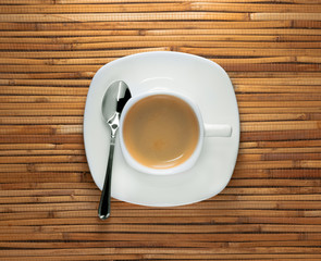 A cup of morning black espresso coffee on saucer with metal spoon on reed background