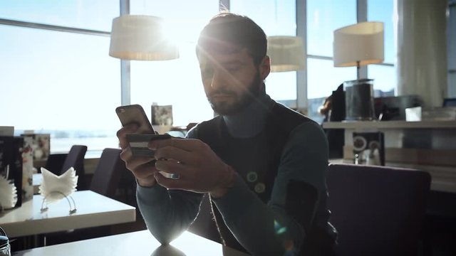    A young bussinesman  paying in online shopping using mobile and credit card,sitting in cafe in a sunny day 