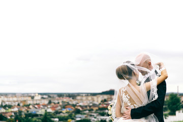 Groom hugs bride while she covers him with her veil