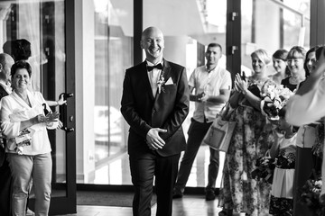 Laughing groom walks in the hall full of guests