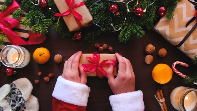 Top hands Santa Claus put a gift wrapped in red ribbon on the table.