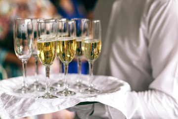 Waiter in white carries champagne flutes on the tray