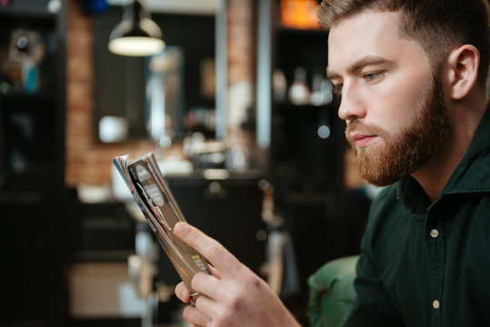 Young man at barbershop reading magazine. - Powered by Adobe