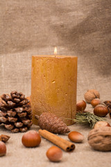 Walnuts, hazelnuts, cinnamon sticks, star anise, cone, candle, fir branch on sackcloth fabric