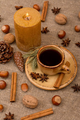 Cup of coffee, walnuts, hazelnuts, cinnamon sticks, star anise, cone, candle, fir branch on sackcloth fabric