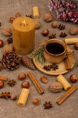 Cup of coffee, cookies, walnuts, hazelnuts, cinnamon sticks, star anise, cone, candle, fir branch on sackcloth fabric