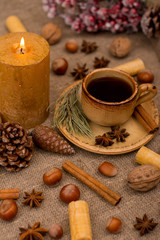 Fototapeta na wymiar Cup of coffee, cookies, walnuts, hazelnuts, cinnamon sticks, star anise, cone, candle, fir branch on sackcloth fabric