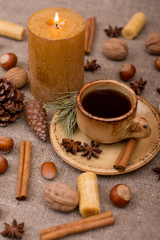 Cup of coffee, cookies, walnuts, hazelnuts, cinnamon sticks, star anise, cone, candle, fir branch on sackcloth fabric
