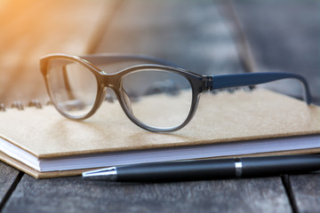 Glasses On Notebook with Pen and Wood Background