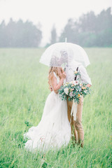 The bride and groom hid from the rain by an umbrella. The bride and groom kissing under an umbrella.