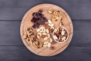 Obraz na płótnie Canvas Granola bars, nuts, and chocolate on wooden cutting board. Top