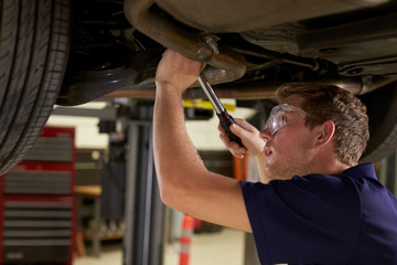 Auto Mechanic Working Underneath Car In Garage