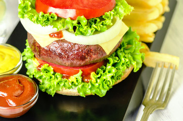 Delicious giant grilled beef burger, large massive thick classic burger with french fries and fresh vegetables..Close up..
