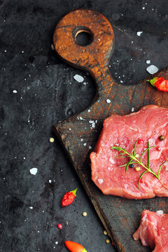 Fresh Raw Beef steak Mignon, with salt, peppercorns, rosemary, pepepr chili.On dark table.Copy space.Selective focus