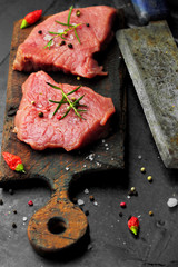 raw beef steak on rustic cutting board, and rustic old knife for meat, rosemary salt and pepepr chili on a dark background.selective focus