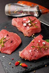 Fresh Raw Beef steak Mignon, with salt, peppercorns, rosemary, pepepr chili.On dark table.Copy space.Selective focus.Pepepr mill and knife decosued on second plan