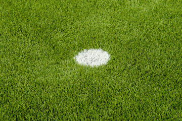 The white penalty point on the artificial green grass soccer field