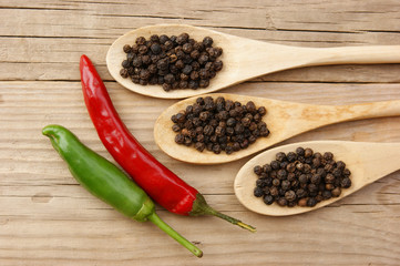 Black and red pepper in wooden spoon on the old board