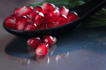 pomegranate seeds in a ceramic spoon and a sprig of rosemary on a dark surface